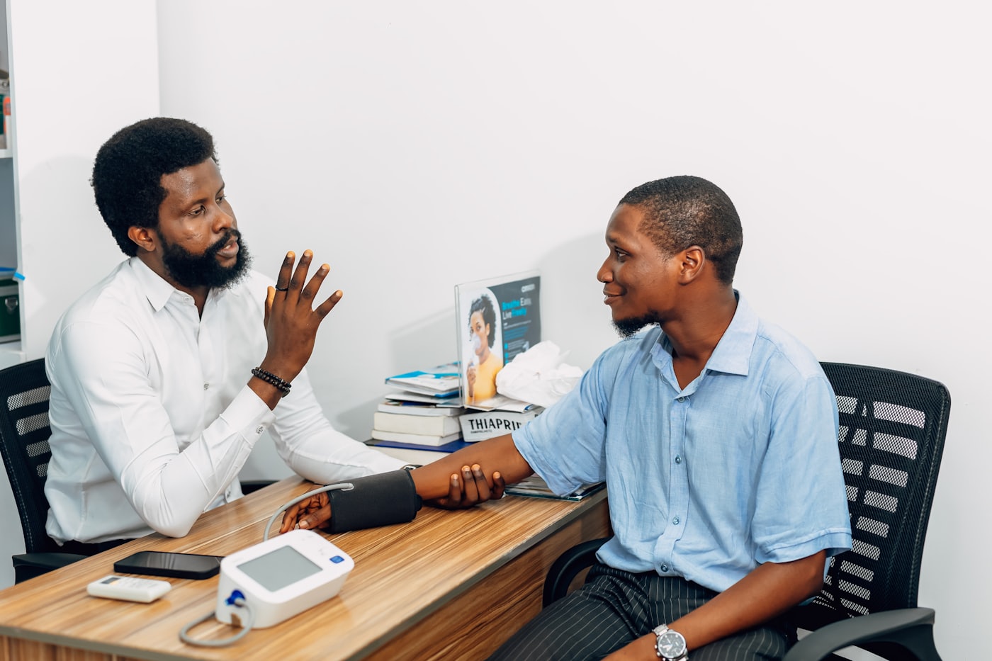 A clinician in a consulting room, explaining something to the person sitting across the desk from him